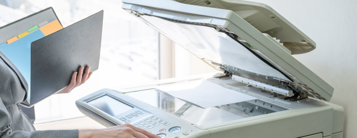 Office employee standing in front of multifunction printer while holding document folder.