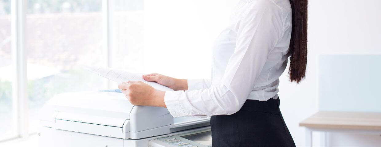 worker stands at a multifunction printer holding documents