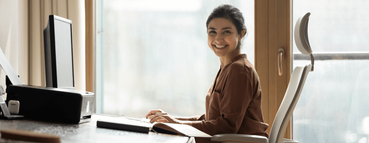 Young woman smiling, sitting on chair at office desk.